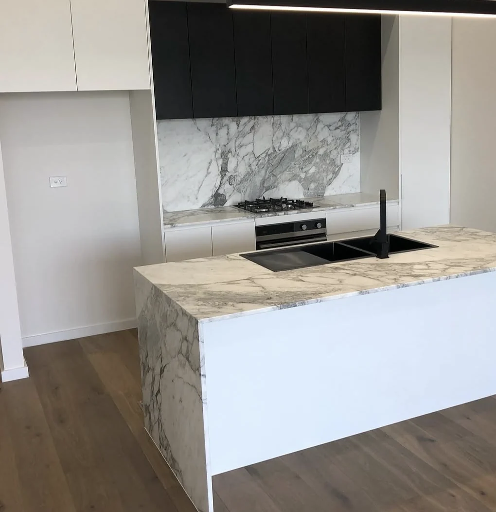 A completed kitchen with a pale stone island and dark cabinetry